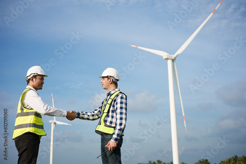 Two asian male engineers handshake with wind turbine and clear blue sky on the background.