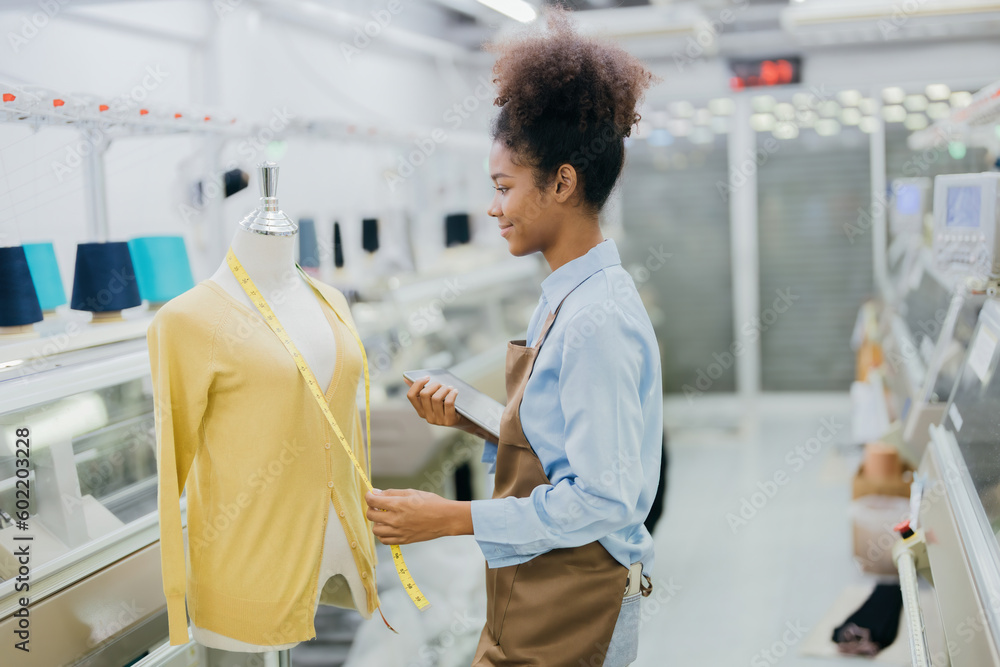 Obraz premium American female designer is designing her clothes and figure with intention There is a tape measure and tablet device. in the weaving industry There was a sewing machine working near her.