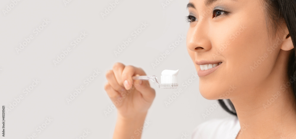 Beautiful Asian woman brushing teeth on light background with space for text Beautiful Asian woman brushing teeth on light background with space for text