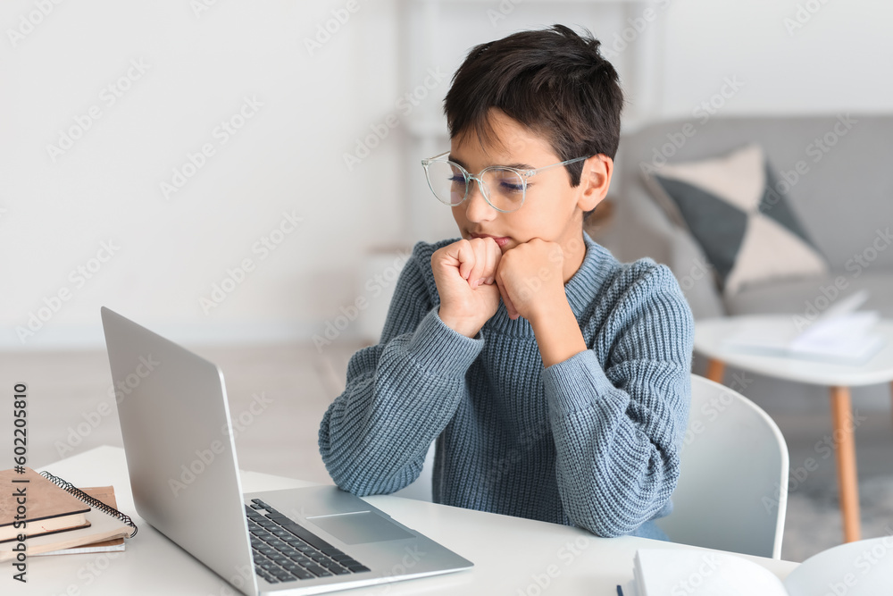 Thoughtful little boy in eyeglasses using laptop at home Thoughtful little boy in eyeglasses using laptop at home