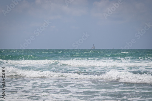 an empty blue sea with waves at Tzuk beach in Tel Aviv, Israel. The sun shines down on the water, creating a sparkling effect. The beach is deserted, with no people or signs of life. 