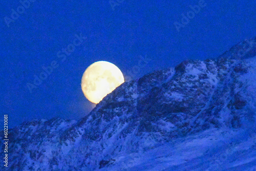 A near full moon is slowly creeping behind a mountain along the norwegian coast on an early winter morning near the town of Bodo. photo