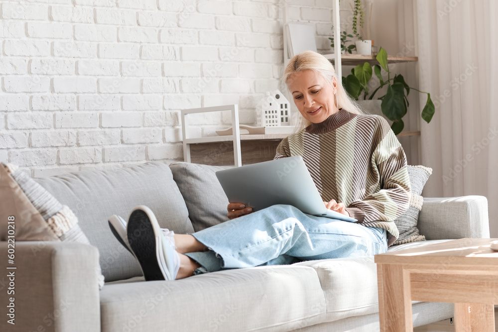 Mature female programmer working with laptop on sofa at home Mature female programmer working with laptop on sofa at home