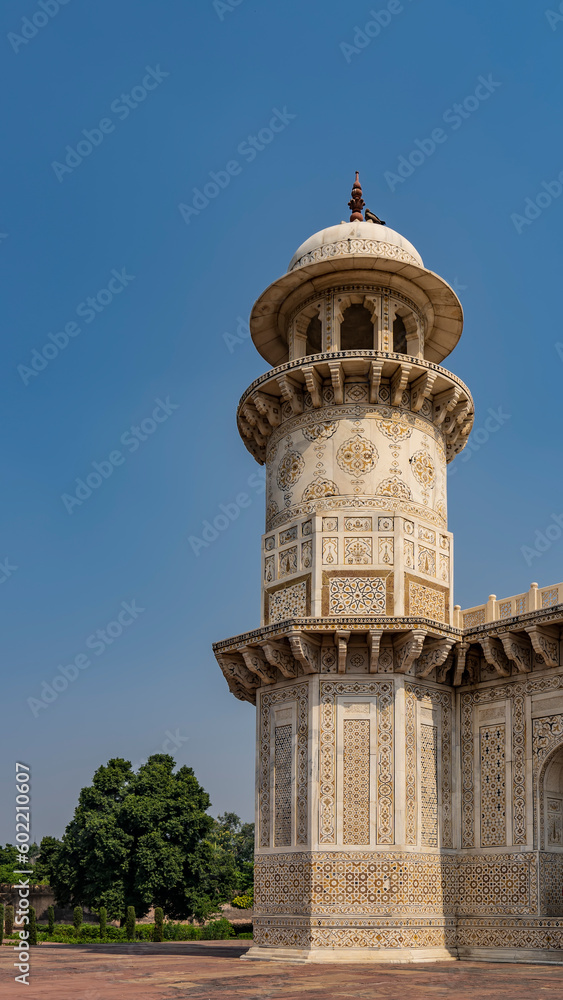 Details of the architecture of the ancient tomb of Itmad-Ud-Daulah. Marble minaret with balconies and a dome against the blue sky. On the walls there are ornaments, inlays of precious stones. India.
