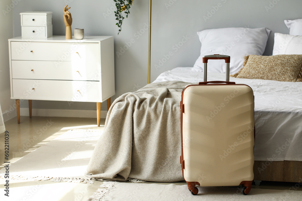 Big suitcase near bed in light room - obrazy, fototapety, plakaty 