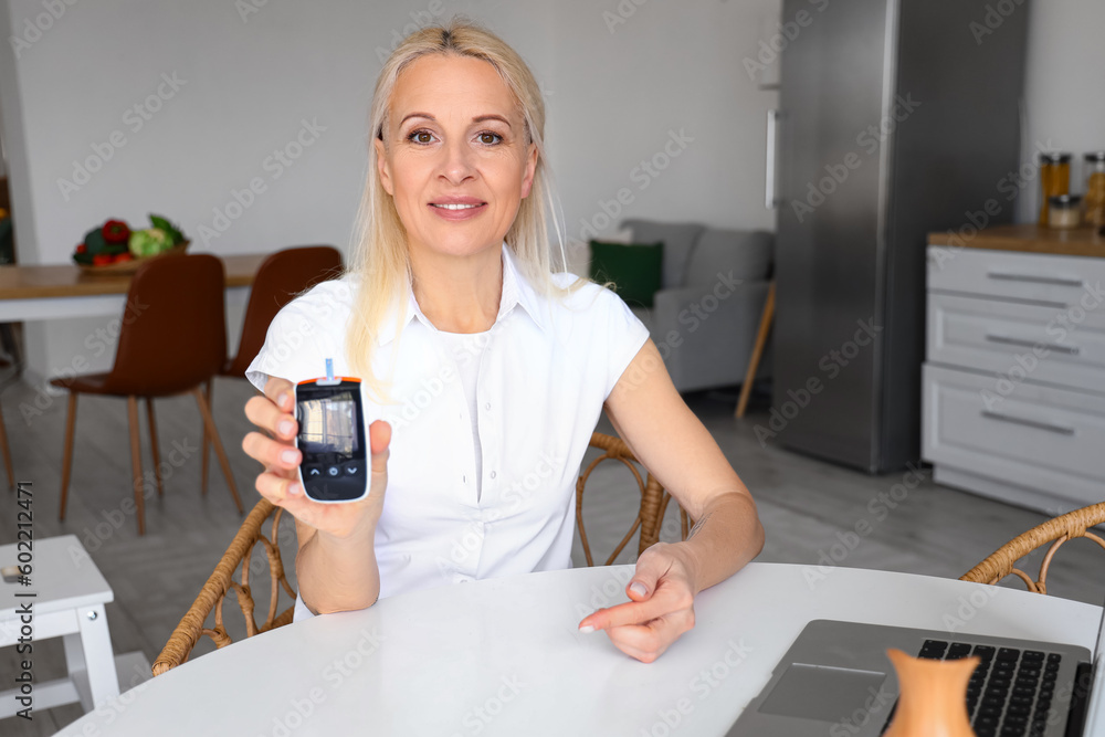 Mature diabetic woman with glucometer in kitchen Mature diabetic woman with glucometer in kitchen
