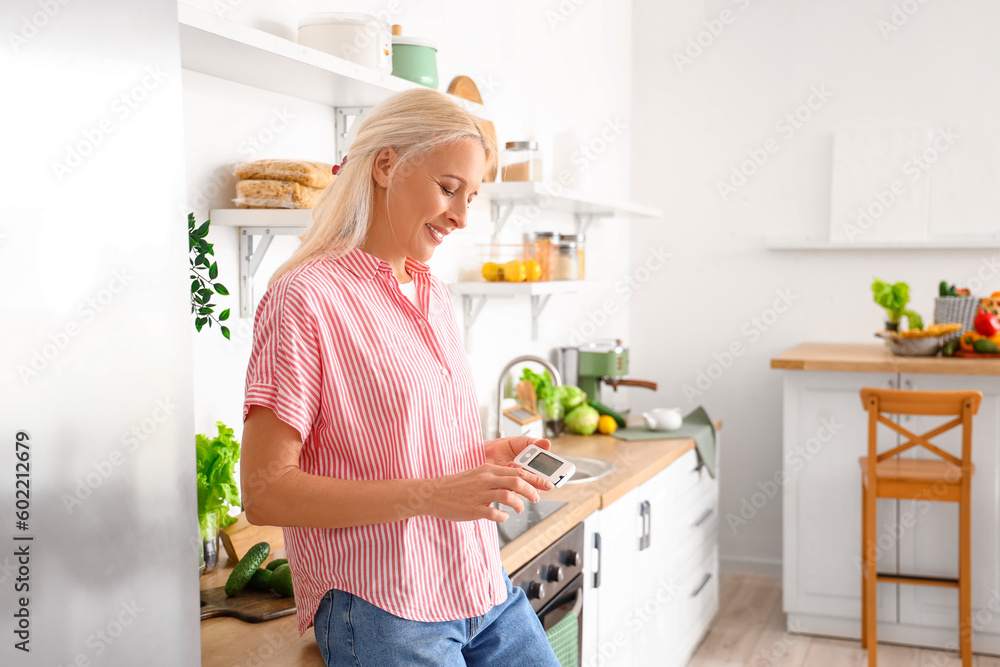 Mature diabetic woman measuring blood sugar level with glucometer in kitchen Mature diabetic woman measuring blood sugar level with glucometer in kitchen