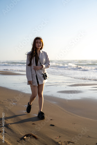 A young woman in a white jacket and black shorts, walking along the windy shoreline at sunset on a beach in Uchinada Town, Ishikawa Prefecture. photo