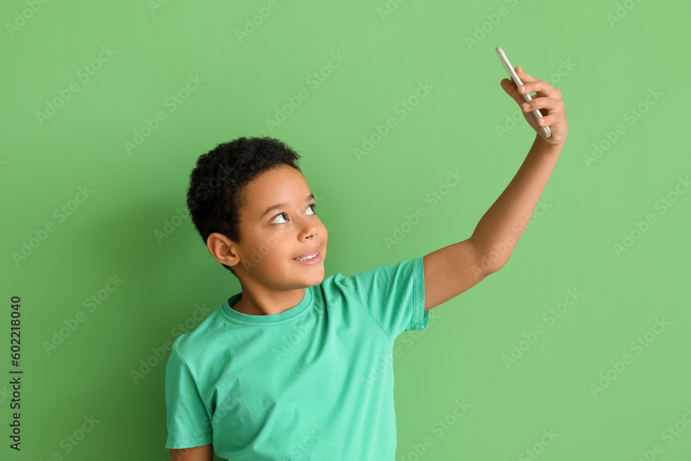 Little African-American boy with mobile phone taking selfie on green background. Children's Day celebration Little African-American boy with mobile phone taking selfie on green background. Children's Day celebration