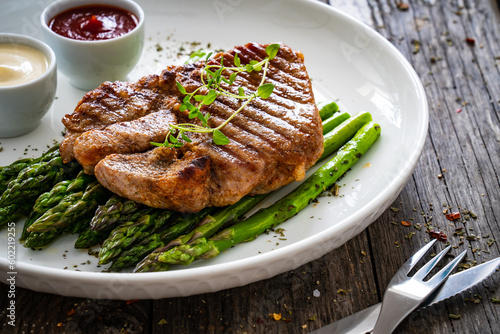 Barbecued pork neck and asparagus on wooden table