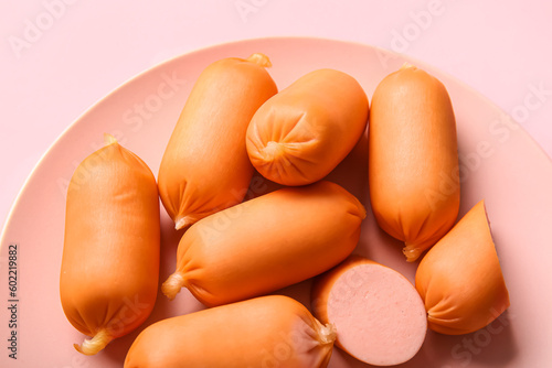 Plate of tasty boiled sausages on pink background