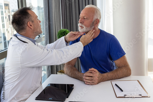 Doctor checking sore throat or thyroid glands of a senior patient by touching neck in hospital office. Thyroid cancer prevention concept photo