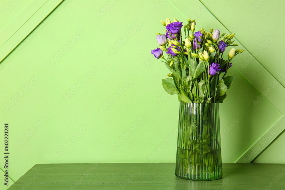 Vase with eustoma flowers on table near green wall Vase with eustoma flowers on table near green wall