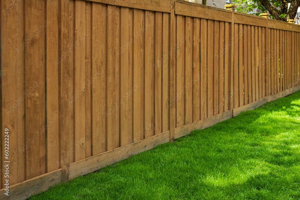 Nice new wooden fence around house. Wooden brown fence with green grass lawn. Street photo Nice new wooden fence around house. Wooden brown fence with green grass lawn. Street photo
