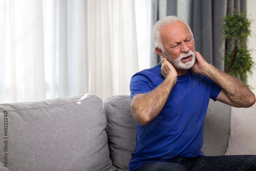 Senior man suffering from neck pain sitting on sofa at home Senior man suffering from neck pain sitting on sofa at home