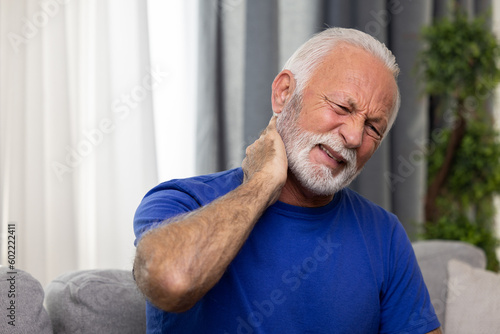 Senior man suffering from neck pain sitting on sofa at home
