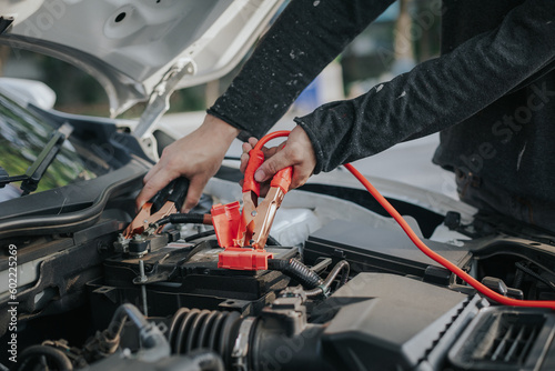 Close-up of auto mechanic charging car battery with electric rail jumper cables