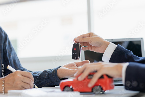 Closing sale. Asian customer signing car insurance paperwork or lease contract or agreement. Buy or sell a new or used car with car keys on the table.