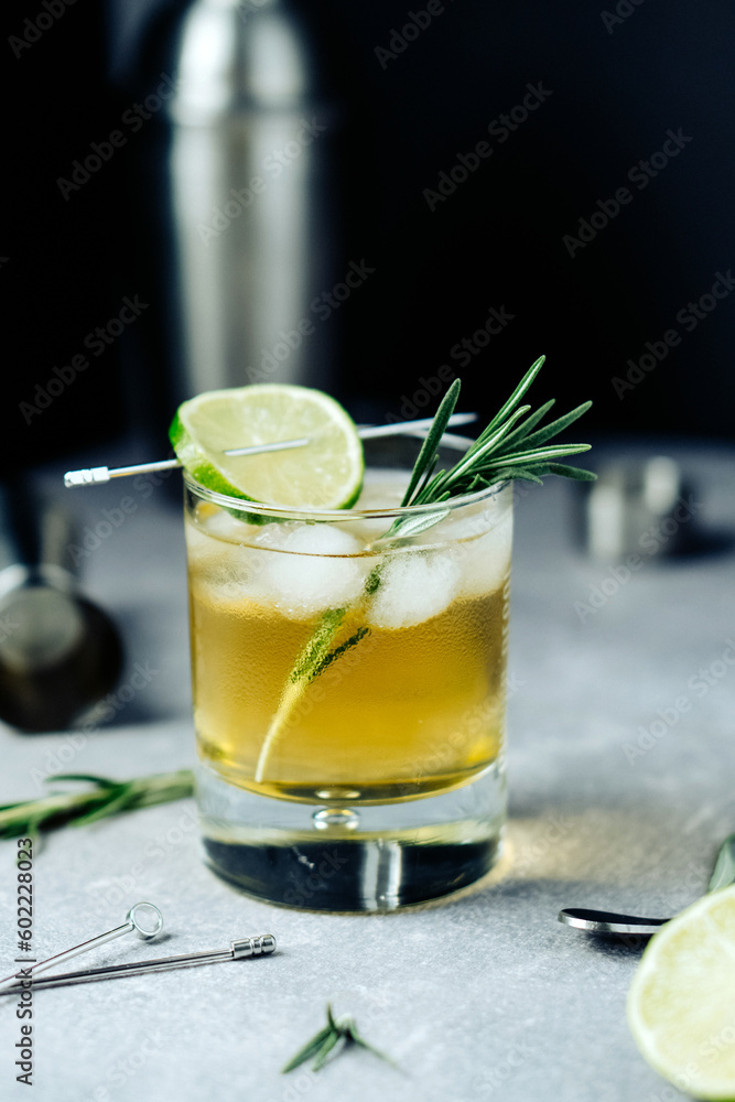 Fototapeta premium Alcohol cocktail with lime slice rosemary ice and cocktail shaker on black background. Party time