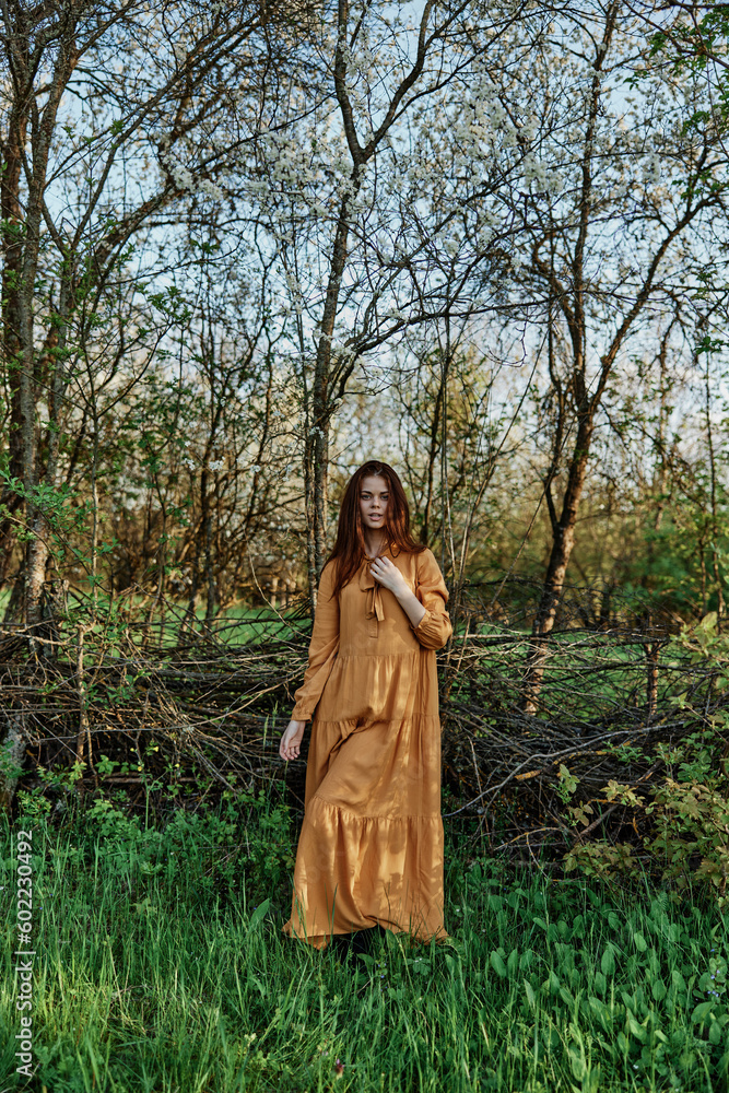 vertical photo of a beautiful, elegant woman in a stylish orange dress standing in the countryside in the shade of trees vertical photo of a beautiful, elegant woman in a stylish orange dress standing in the countryside in the shade of trees