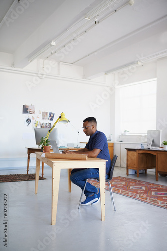 Creative, office or black man typing on laptop working on a blog project, digital or online research. Coworking, planning or focused African designer working on website in startup company agency