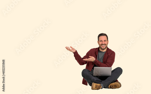 Cheerful young male professional showing copy space for marketing while working over laptop on background. Businessman happily gesturing and advertising while sitting with legs crossed