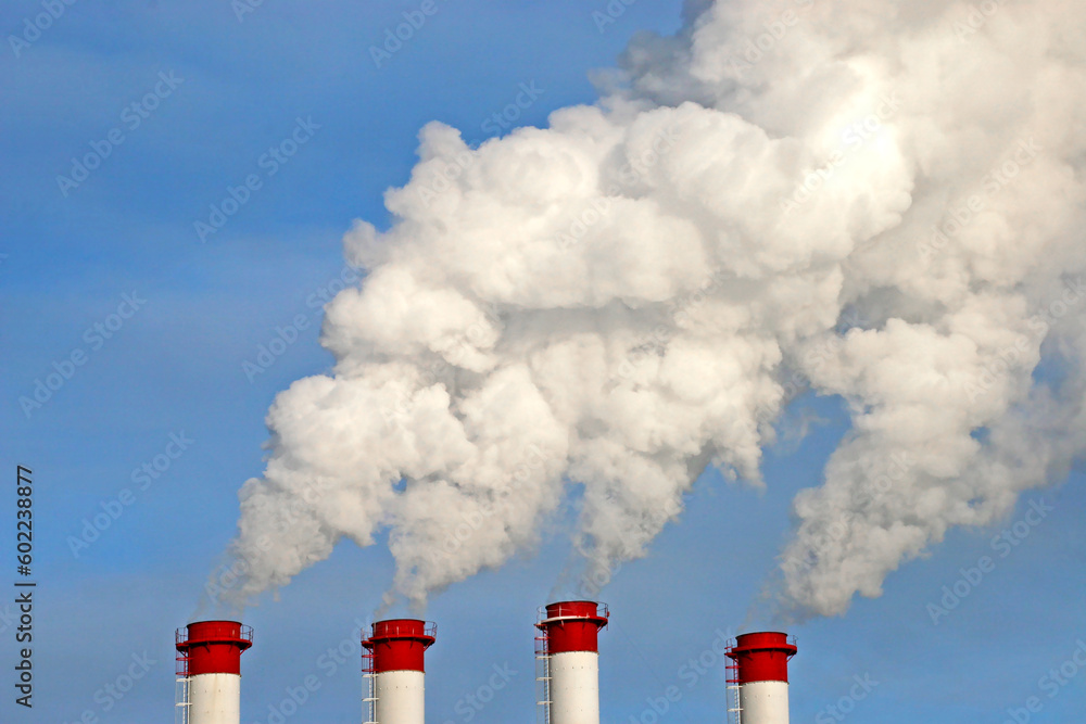 Industrial chimneys with white smoke against blue sky. Tall pipes with steam on a winter day.