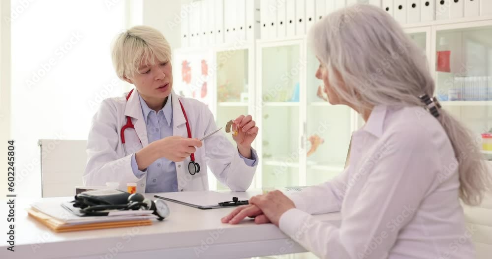 Female doctor explains correct usage of hearing aid to mature client. Woman listens attentively while sitting at consultation with specialist slow motion Female doctor explains correct usage of hearing aid to mature client. Woman listens attentively while sitting at consultation with specialist slow motion