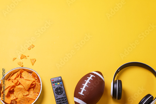 TV remote, a bowl of chips and a headphones on a yellow background. American football and super bowl concept.