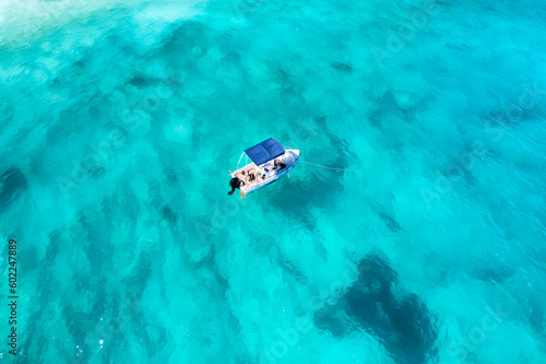 Aerial view of a small motorboat floating on a turquoise crystal clear transparent water.