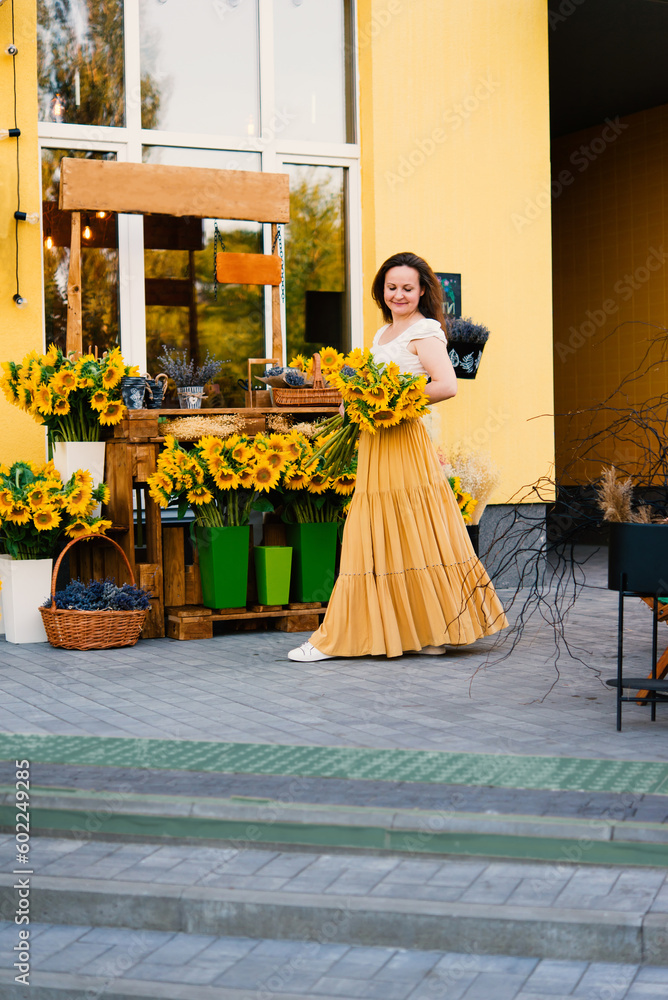 Naklejka premium Elegant smiling woman with a bouquet of sunflowers flowers near a cafe - a flower shop.