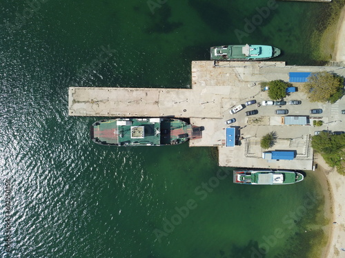 Ferry boat crossing the sea, carrying cars and passengers. Cars drive off the deck onto the port. Top-down aerial drone view Ferry on the lake, transporting cars: deck of a boat carrying vehicles.