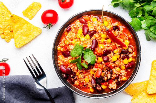 Chili con carne with minced beef, red beans, paprika, sweet corn and hot peppers in spicy tomato sauce, tex-mex cuisine dish, white table background, top view