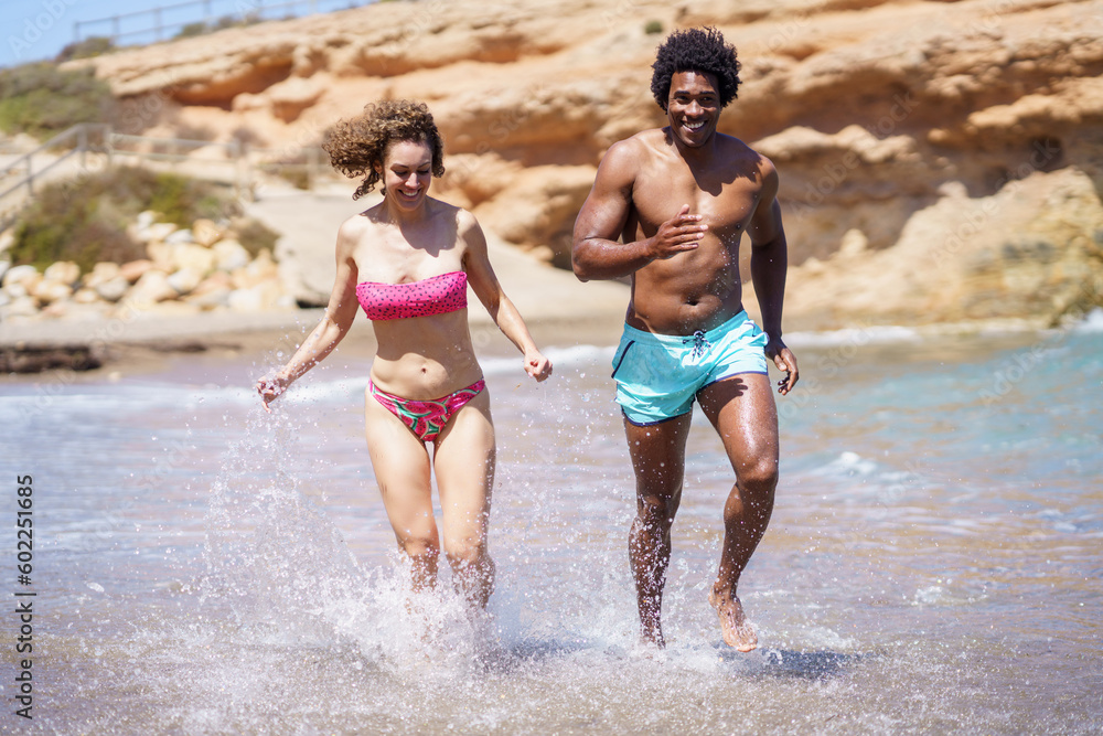 Happy multiracial couple sprinting in seawater in sunlight