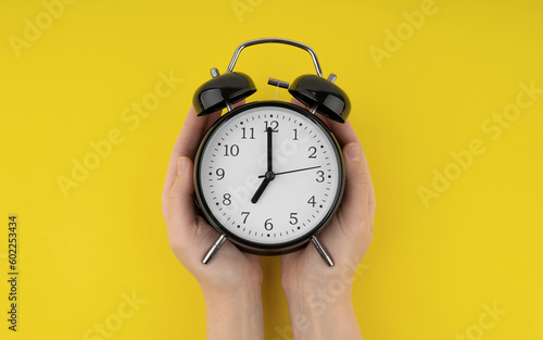 Woman's hands holding a black alarm clock on a yellow background