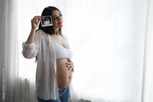 Obraz na płótnie Pregnant woman standing hold strokes hold ultrasound photo of belly tummy fetus abdomen enjoying pregnancy