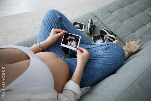Obraz na płótnie Pregnant woman sitting hold ultrasound photo of belly strokes tummy fetus abdomen enjoying pregnancy