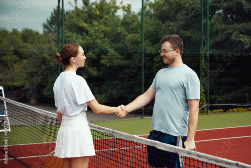 Young tennis players giving fist bump with fist before playing court game. Cheerful man and girl greeting