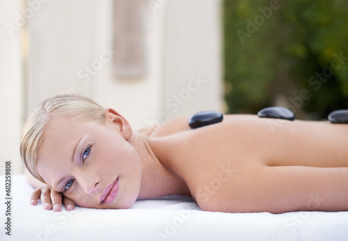 Woman at spa, hot stone and portrait massage for healing, wellness and holistic treatment at luxury resort. Stress relief, zen and female person with rocks on back in self care or relax muscle heath