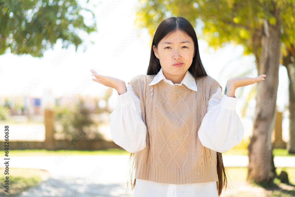 Pretty Chinese woman at outdoors having doubts while raising hands Pretty Chinese woman at outdoors having doubts while raising hands