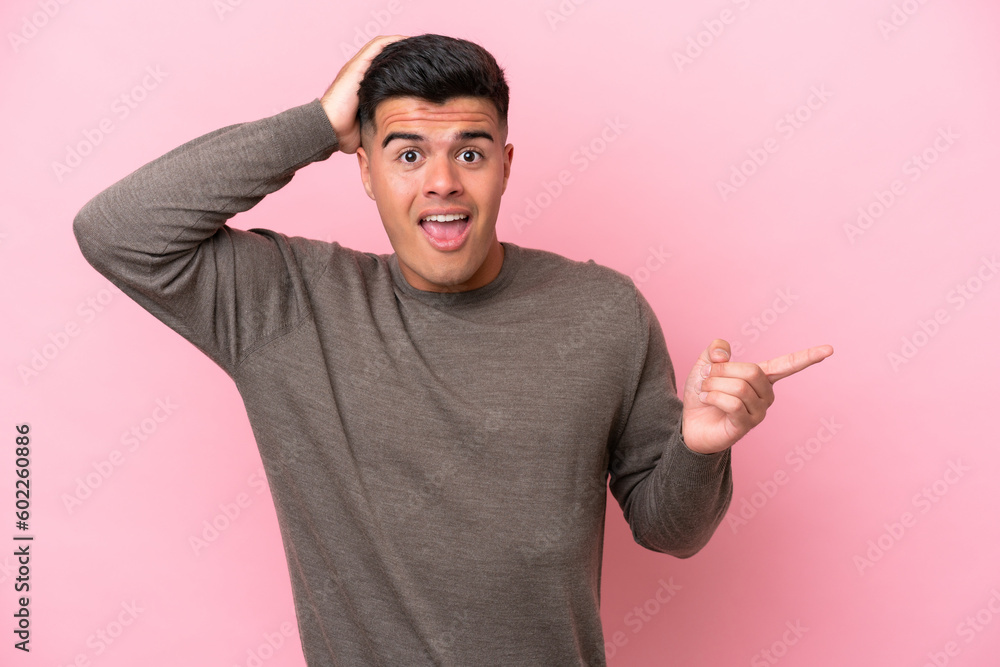 Young caucasian handsome man isolated on pink background surprised and pointing finger to the side Young caucasian handsome man isolated on pink background surprised and pointing finger to the side