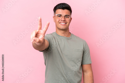 Young caucasian handsome man isolated on pink background smiling and showing victory sign