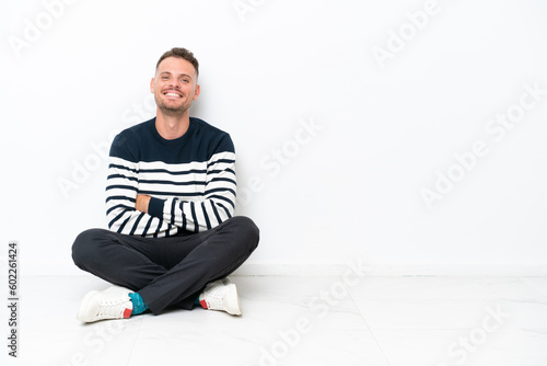 Young man sitting on the floor isolated on white background keeping the arms crossed in frontal position