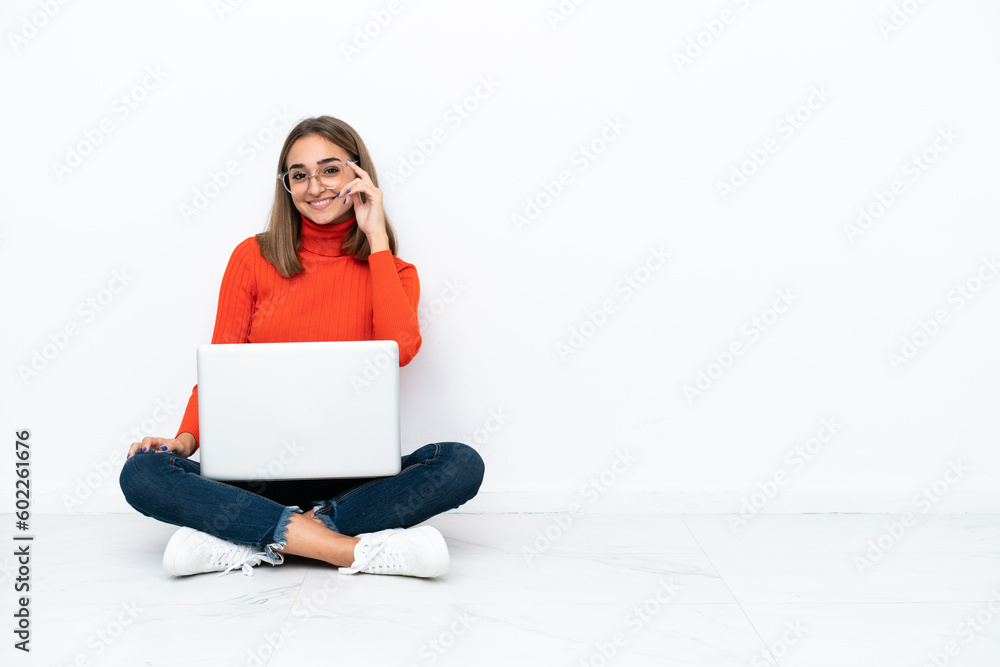 Young caucasian woman sitting on the floor with a laptop with glasses and happy Young caucasian woman sitting on the floor with a laptop with glasses and happy