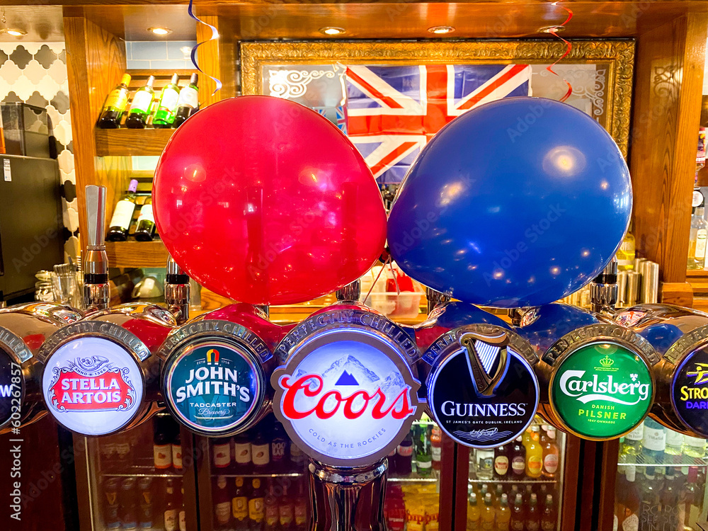 Beer pumps on a bar in a pub in The UK decorated with red and blue