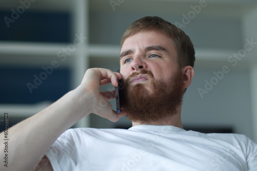 Portrait of young angry sad upset frustrated man, dissatisfied unhappy guy talk, swear on cell mobile phone, calling on smartphone at home in living room on couch 