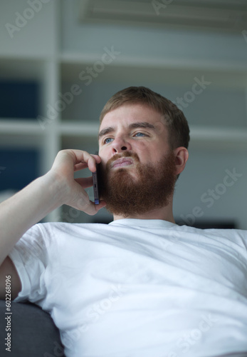 Portrait of young angry sad upset frustrated man, dissatisfied unhappy guy talk, swear on cell mobile phone, calling on smartphone at home in living room on couch. Vertical photo 