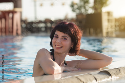 Portrait of a brunette woman in the water at the side of the pool.