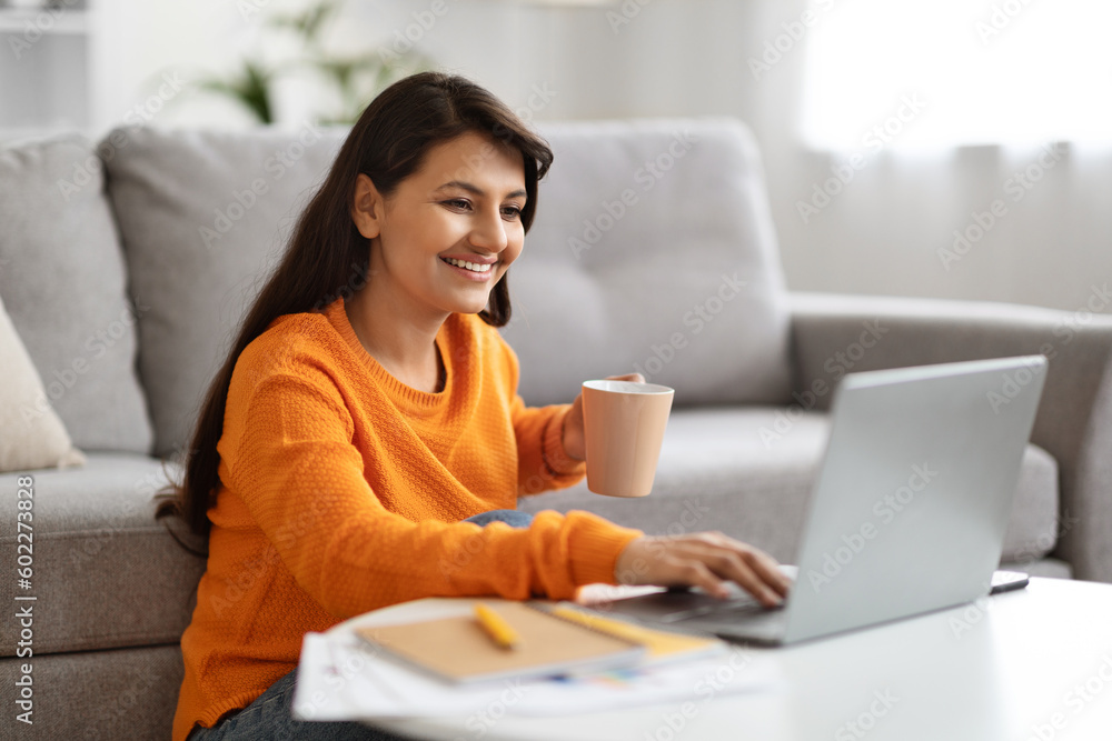 Happy indian woman freelancer working on laptop, home interior Happy indian woman freelancer working on laptop, home interior