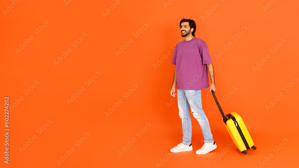 Happy young eastern man with luggage looking at empty space